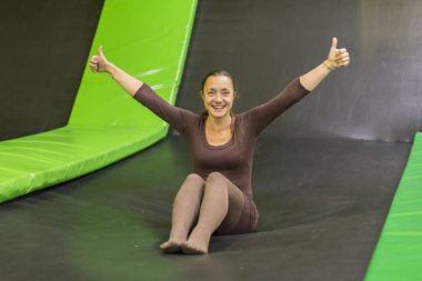genç kadın kahverengi uyum içinde elbise trambolin Center'da trambolin üzerinde. dikey fotoğraf. Mutlu kız trambolin üzerinde. Trambolin üzerinde mutlu genç kadın