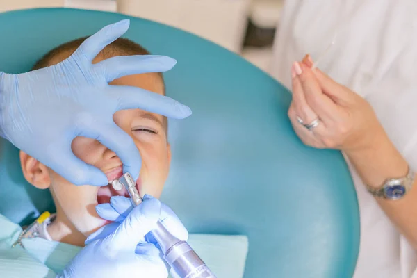Tandläkare behandlar en pojkes tänder. Tandläkaren undersöker pojkens tänder i klinik. En liten patient i stol ler. Dantist behandlar tänder — Stockfoto