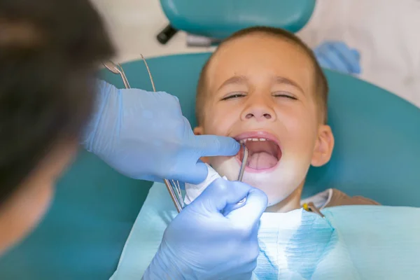 En liten pojke på en tandläkarens mottagning i en tandvårdsklinik. Barnens tandvård, Pediatric Dentistry. En kvinnlig tandläkare behandlar tänderna av en pojke i skolåldern. Oral hälsa och hygien — Stockfoto
