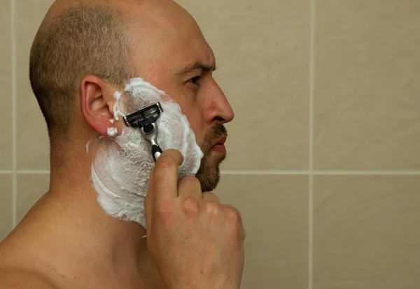 Een man die zijn gezicht scheert met het scheermesje door scheerschuim. Mannen huidverzorgingsconcept. — Stockfoto