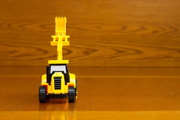 Tractor infantil amarillo con un cubo elevado sobre fondo marrón — Foto de Stock