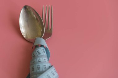 kaşık ve çatal mezura pembe bir arka plan üzerinde sarılı. Doğru beslenme. Tıbbi açlık. Diyet kilo kaybı kavramı için. Metin için boş alan