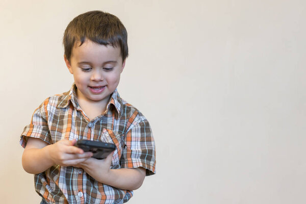 Портрет улыбающегося мальчика, держащего мобильный телефон изолированным на светлом фоне. милый ребенок играет в игры на смартфоне. копировальное пространство

