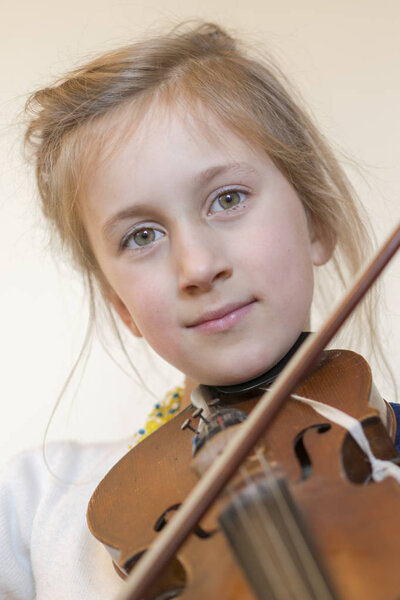 Close up of a child playing violin on isolated light background. Portrait of girl with string and playing violin. Portrait of the little violinist. Beautiful gifted little girl playing on violin