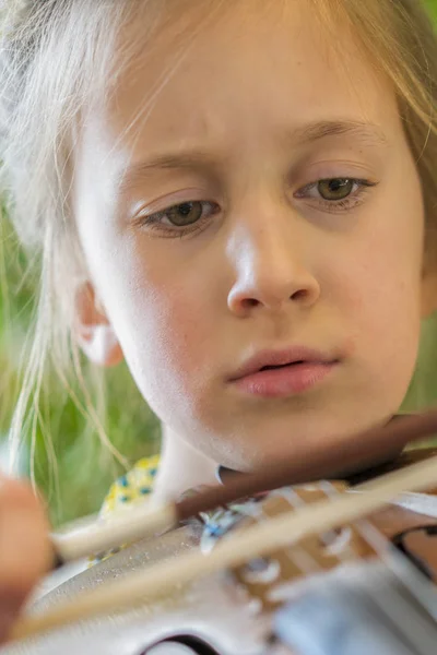 Крупный план ребенка, играющего на скрипке на зеленом фоне. Портрет девушки со струной и игрой на скрипке. Портрет маленькой скрипачки. Красивая одаренная девочка играет на скрипке — стоковое фото