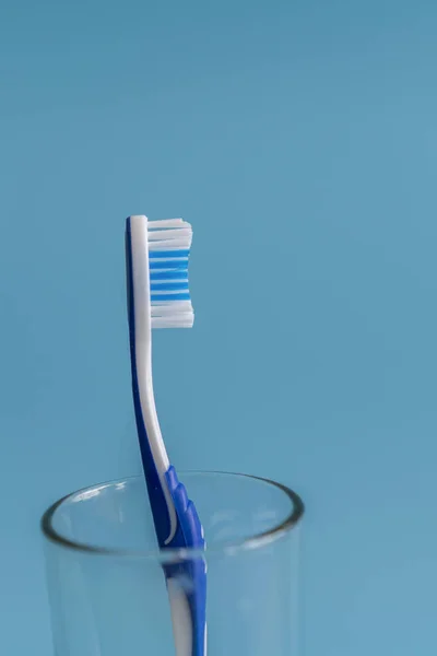 Escova de dentes, em um copo no fundo azul. foto vertical — Fotografia de Stock
