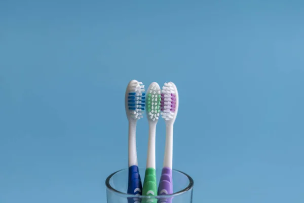 Conjunto de escovas de dentes em vidro sobre fundo azul. Copo com escovas de dentes contra fundo de cor. Cuidados dentários — Fotografia de Stock