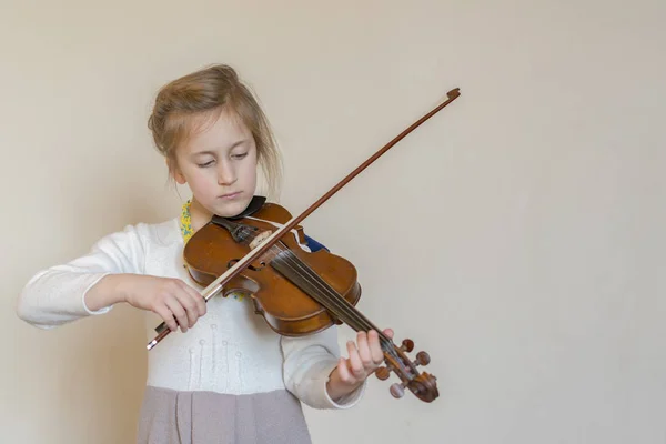 Cute little girl in a beautiful dress playing violin. Joyful and happy emotions. Training. Education. School. Aesthetic training. Portrait of a young girl playing violin on light background.