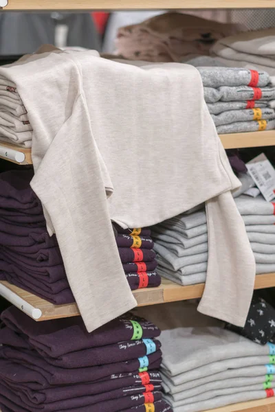 Neatly folded clothes. Rack of clothes with warm. Wooden cabinet with a stack of sweaters. Coloured clothing. Neat stacks of folded clothing on the shop shelves. vertical photo.