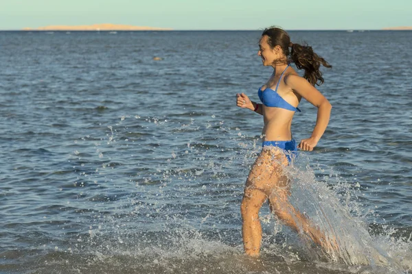 一个性感的年轻黑发女人或女孩穿着比基尼在一个空旷的热带海滩上跑来跑去 天空是蓝色的 在海边奔跑的年轻妇女 — 图库照片