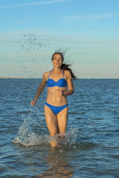 セクシーな若いブルネットの女性または捨てられた熱帯のビーチと青い空でサーフィンを介して実行されているビキニを着ている少女 海沿い走っている若い女性 垂直写真 — ストック写真