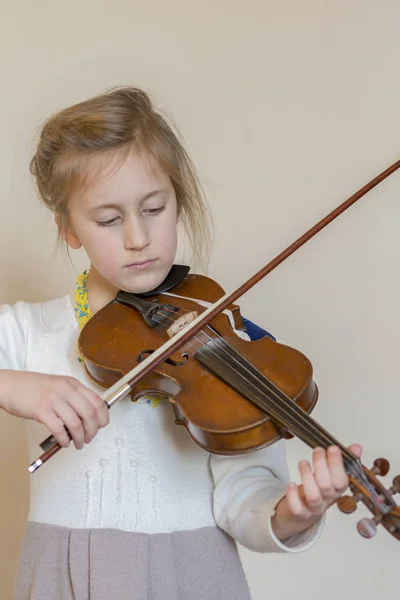 Cute little girl in a beautiful dress playing violin. Joyful and happy emotions. Training. Education. School. Aesthetic training. Portrait of a young girl playing violin on light background.