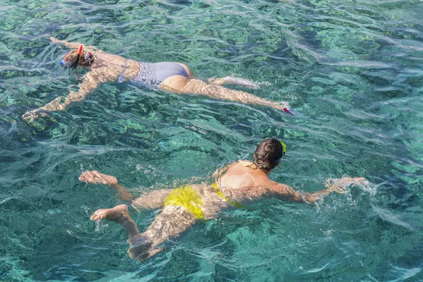 Married couple snorkeling in tropical water on vacation. Woman swimming in blue sea. Snorkeling girl in full-face snorkeling mask. People in flippers and masks in the clear sea.