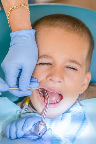歯科診療所における少年の歯を調べること 歯科用椅子笑顔で小さな患者 Dantist 歯を扱います 歯科医のオフィスで小さな男の子の歯の治療の歯科医のビューを閉じます 垂直写真 — ストック写真