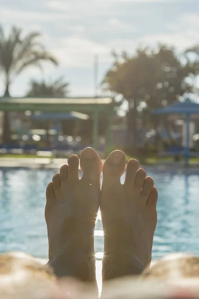 Man\'s feet on the background of a swimming pool. man relaxing by the pool, men\'s feet on the pool background. toned. vertical photo.
