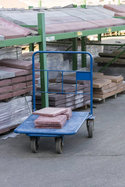 Store building materials and street tiles. Display of decorative paving stones and road bricks at a stoneyard shop organized on display pallets for sale stored on wooden shelves outdoors.