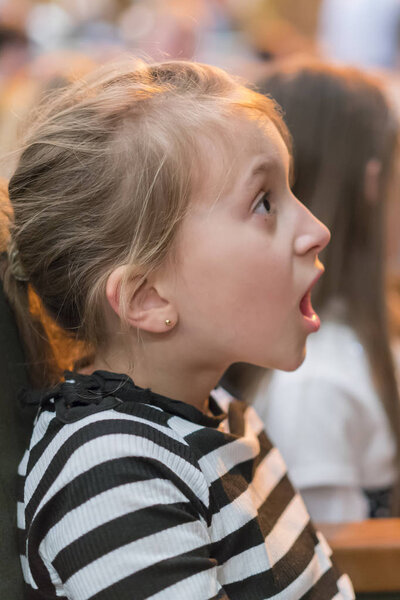 little girl sitting on armchairs at cinema or in the theater. The girl with great interest in the theater. Beautiful little girl sitting in cinema theatre. srlrcted focus.