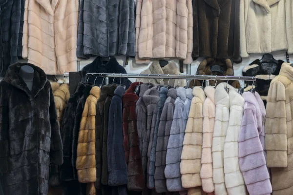 Luxury mink coats. Pink, grey, dark grey, pearl color fur coats on showcase of market. Best gift for a woman. Outerwear. Close up.