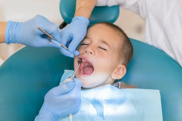 歯科医は、少年の歯を扱っています。歯科診療所における少年の歯を調べること。歯科用椅子笑顔で小さな患者。Dantist 歯を扱う — ストック写真