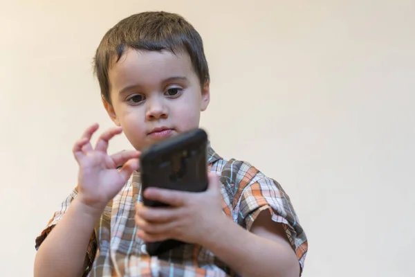 Портрет усміхненого маленького хлопчика, який тримає мобільний телефон ізольовано на світлому фоні. мила дитина грає в ігри на смартфоні. копіювання простору — стокове фото