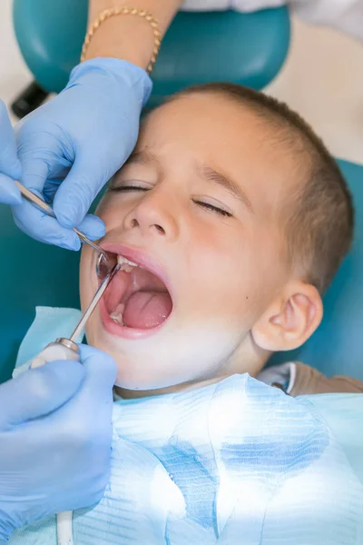Dentysta, badając chłopca zębów w klinice. Mały pacjent w uśmiechy fotela. Uczyć się u wybitnych leczy zęby. zbliżenie dentysta, leczenie zębów małego chłopca w gabinecie stomatologicznym. pionowe zdjęcie — Zdjęcie stockowe