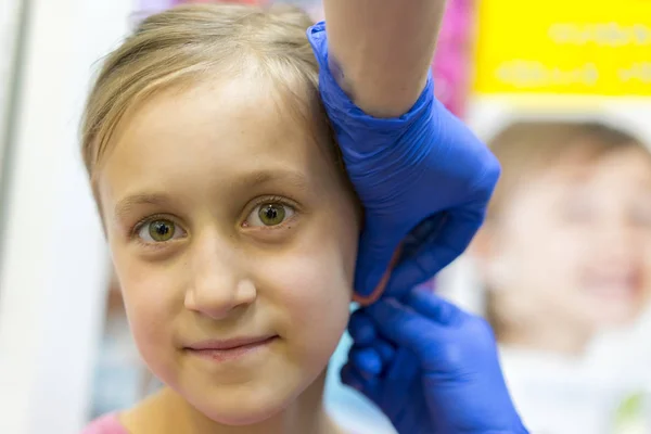 Menina orelha perfurada no salão de beleza. Adorável menina tendo orelha piercing processo com equipamento especial no centro de beleza por médico trabalhador . — Fotografia de Stock