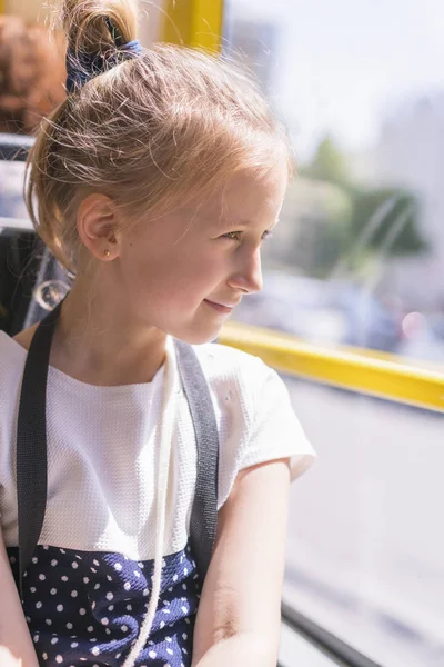En liten flicka åker med buss. Skol flicka sitter i skol bussen och redo för sin första tur. vertikalt Foto — Stockfoto