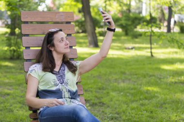 Genç kadın parkta selfie yapıyor. Uzun sarı saçlı seksi genç kadın parkta yaz gününde selfie yapıyor. Neşeli kız parkta yaz gününde selfie yapma. Kopyalama alanı