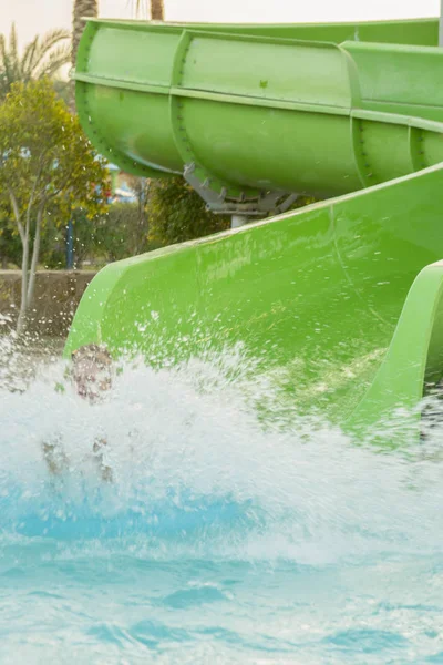 Menino está se divertindo, enquanto passa o tempo no aquapark. Ele está deslizando para baixo da corrediça de água fazendo uma série de salpicos. foto vertical — Fotografia de Stock