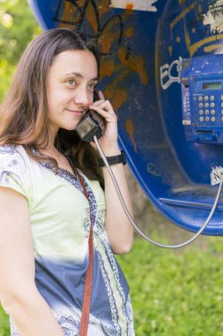 Telefon kulübesinde güzel genç bir kadın. Kız telefon telefonda konuşuyor. kamu telefonla konuşan kadın