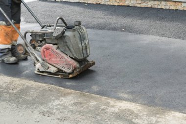 Yol işçileri yolda titreşimli bir Rammer ile asfalt kompakt. Bir yol inşaatı yerinde kompaktör ile çalışan