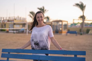 Bankta oturan genç kadın. Mavi bir Bank üzerinde güzel bir gülümseme olan bir kadın. Huzur ve mutluluk kavramı. kopya alanı