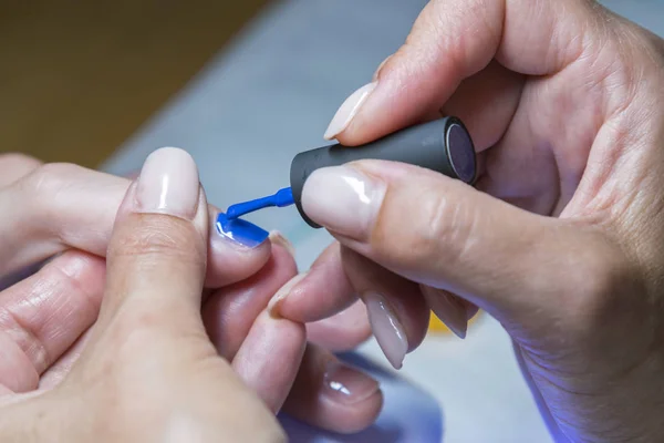 Hermoso proceso de manicura. El esmalte de uñas que se aplica a la mano, el esmalte es de color azul. de cerca — Foto de Stock