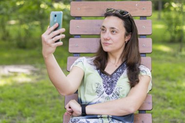 Parkta selfie çeken genç kadın. Uzun sarı saçlı seksi genç kadın parkta yaz günü selfie yapıyor. Parkta yaz günü selfie yapan neşeli kız. kopya alanı. yakın çekim