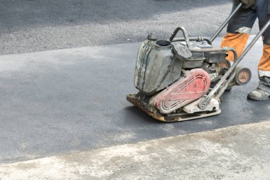 Yol işçileri yolda titreşimli bir Rammer ile asfalt kompakt. Bir yol inşaatı yerinde kompaktör ile çalışan