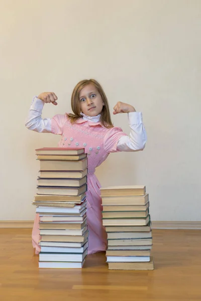 Concepto El poder del conocimiento. Una chica con un montón de libros muestra su fuerza. Concepto educativo. espacio de copia. foto vertical —  Fotos de Stock