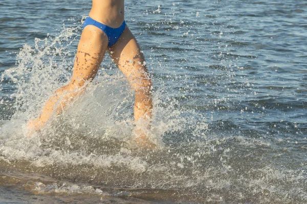 Seorang wanita muda atau gadis berambut cokelat seksi mengenakan bikini berjalan melalui ombak di pantai tropis sepi dengan langit biru. Wanita muda berjalan oleh laut — Stok Foto