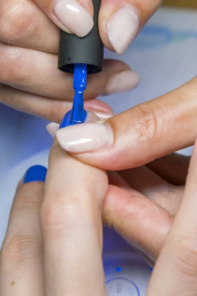 Hermoso proceso de manicura. El esmalte de uñas que se aplica a la mano, el esmalte es de color azul. Primer plano. foto vertical — Foto de Stock