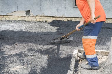 İşçi adam sarı güneş ışını ışık döşeme asfalt yol tamir yol bırakır. Tulumlu bir adam kürekle asfalt döşeyen..