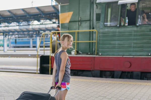 Девушка-подросток на вокзале возле локомотива. девушка тащит большой чемодан на платформе — стоковое фото