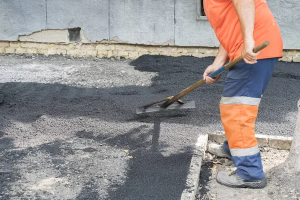 Hombre trabajador pone asfalto carretera reparación carretera pavimentación luz de rayos de sol amarillo. Un hombre en overol está poniendo asfalto con una pala . — Foto de Stock