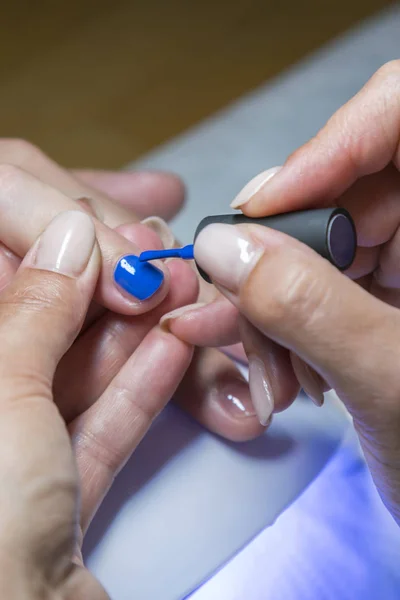 Hermoso proceso de manicura. El esmalte de uñas que se aplica a la mano, el esmalte es de color azul. De cerca. foto vertical — Foto de Stock