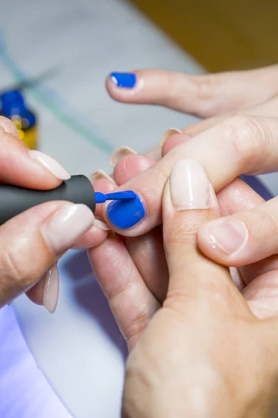 Hermoso proceso de manicura. El esmalte de uñas que se aplica a la mano, el esmalte es de color azul. Primer plano. foto vertical — Foto de Stock