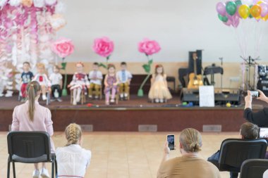 İlkokulda çocuk partisi. Anaokulu sahnede genç çocuklar ön ebeveynler görünür. Bulanık