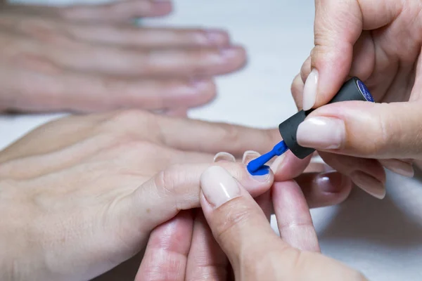 Hermoso proceso de manicura. El esmalte de uñas que se aplica a la mano, el esmalte es de color azul. de cerca — Foto de Stock