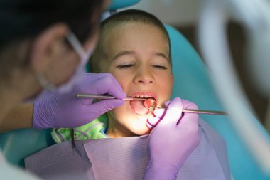 Çocuk diş hekimi diş kliniğinde diş hekimi sandalyesinde küçük bir erkek dişleri muayene. Dişçilik ofisinde dişçisi olan bir çocuk. Klinikte diş hekimi muayenesi küçük çocuğun dişleri yakın