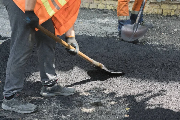 Hombre trabajador pone asfalto carretera reparación carretera pavimentación luz de rayos de sol amarillo. Un hombre en overol está poniendo asfalto con una pala — Foto de Stock