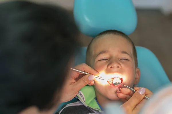 Pediatrisk tandläkare undersöka en liten pojkar tänder i tandläkare stol på tandkliniken. Ett barn med tandläkar mottagning. Närbild av pojke med sina tänder undersökas av en tandläkare — Stockfoto