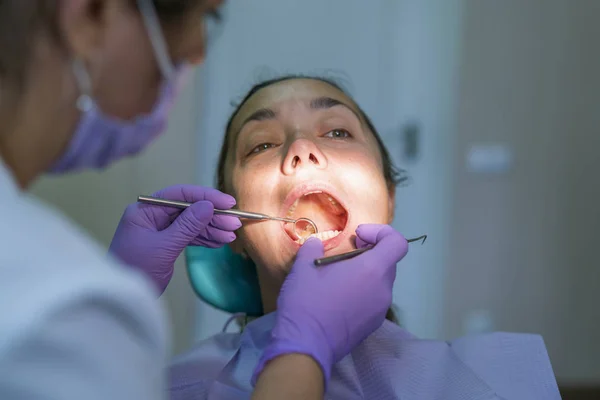 Dentist and patient in dentist office. Close-up of dental drill use for patient teeth in dentistry office in a dental treatment procedure. Woman having teeth examined at dentists.