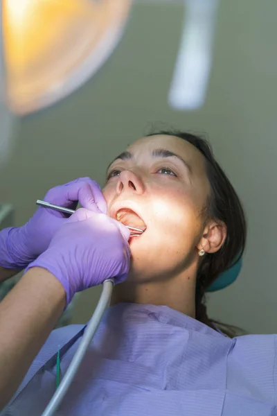 Dentist and patient in dentist office. Close-up of dental drill use for patient teeth in dentistry office in a dental treatment procedure. Woman having teeth examined at dentists. ertical photo